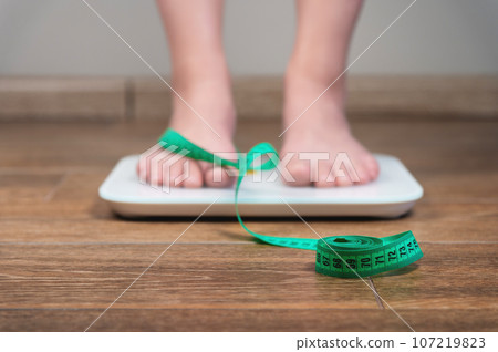 Unrecognizable woman standing on the scales, checking her weight, focused on the measuring tape 107219823