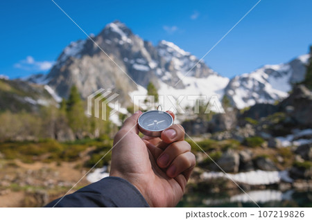 Snow-capped mountains and a tourist hand with an old metal compass in the foreground. Nature reserve, landscape photography Snow-capped mountains and a tourist hand with an old metal compass in the foreground. Nature reserve, landscape photography 107219826