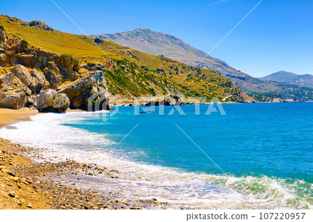 View of sandy beach of Preveli, Crete island, Greece on clear sunny day. Travel destination, river and clear Lybian sea waters, forest, palm trees, gorge, blue sky with clouds. Tourist swim and 107220957