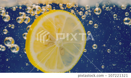 Underwater of freshly squeezed sweetened lemonade which raw lemons slice falling in soda water against dark blue or black background. Close up lemonade or Highball lemon cocktail cold refreshing drink Underwater of freshly squeezed sweetened lemonade which raw lemons slice falling in soda water against dark blue or black background. Close up lemonade or Highball lemon cocktail cold refreshing drink 107221321