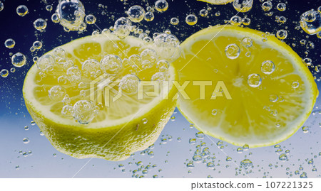 Underwater of freshly squeezed sweetened lemonade which raw lemons slice falling in soda water against dark blue or black background. Close up lemonade or Highball lemon cocktail cold refreshing drink Underwater of freshly squeezed sweetened lemonade which raw lemons slice falling in soda water against dark blue or black background. Close up lemonade or Highball lemon cocktail cold refreshing drink 107221325