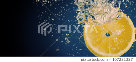 Underwater of freshly squeezed sweetened lemonade which raw lemons slice falling in soda water against dark blue or black background. Close up lemonade or Highball lemon cocktail cold refreshing drink 107221327
