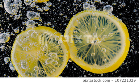 Underwater of freshly squeezed sweetened lemonade which raw lemons slice falling in soda water against dark blue or black background. Close up lemonade or Highball lemon cocktail cold refreshing drink Underwater of freshly squeezed sweetened lemonade which raw lemons slice falling in soda water against dark blue or black background. Close up lemonade or Highball lemon cocktail cold refreshing drink 107221329