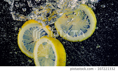 Underwater of freshly squeezed sweetened lemonade which raw lemons slice falling in soda water against dark blue or black background. Close up lemonade or Highball lemon cocktail cold refreshing drink Underwater of freshly squeezed sweetened lemonade which raw lemons slice falling in soda water against dark blue or black background. Close up lemonade or Highball lemon cocktail cold refreshing drink 107221332