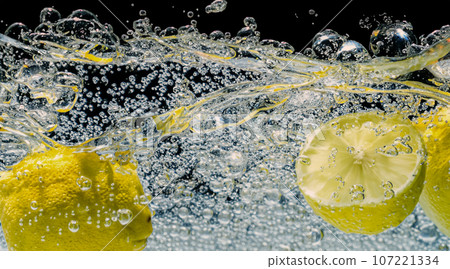 Underwater of freshly squeezed sweetened lemonade which raw lemons slice falling in soda water against dark blue or black background. Close up lemonade or Highball lemon cocktail cold refreshing drink Underwater of freshly squeezed sweetened lemonade which raw lemons slice falling in soda water against dark blue or black background. Close up lemonade or Highball lemon cocktail cold refreshing drink 107221334