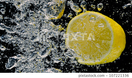 Underwater of freshly squeezed sweetened lemonade which raw lemons slice falling in soda water against dark blue or black background. Close up lemonade or Highball lemon cocktail cold refreshing drink Underwater of freshly squeezed sweetened lemonade which raw lemons slice falling in soda water against dark blue or black background. Close up lemonade or Highball lemon cocktail cold refreshing drink 107221336