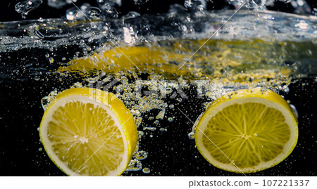 Underwater of freshly squeezed sweetened lemonade which raw lemons slice falling in soda water against dark blue or black background. Close up lemonade or Highball lemon cocktail cold refreshing drink 107221337
