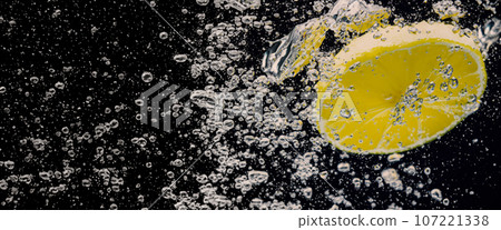 Underwater of freshly squeezed sweetened lemonade which raw lemons slice falling in soda water against dark blue or black background. Close up lemonade or Highball lemon cocktail cold refreshing drink Underwater of freshly squeezed sweetened lemonade which raw lemons slice falling in soda water against dark blue or black background. Close up lemonade or Highball lemon cocktail cold refreshing drink 107221338