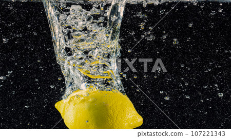 Underwater of freshly squeezed sweetened lemonade which raw lemons slice falling in soda water against dark blue or black background. Close up lemonade or Highball lemon cocktail cold refreshing drink Underwater of freshly squeezed sweetened lemonade which raw lemons slice falling in soda water against dark blue or black background. Close up lemonade or Highball lemon cocktail cold refreshing drink 107221343