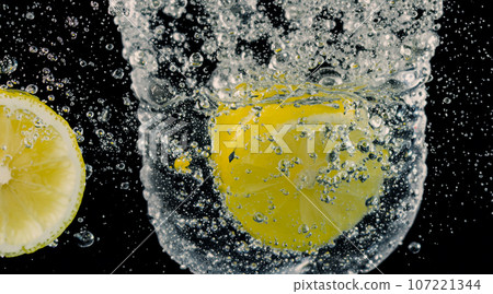 Underwater of freshly squeezed sweetened lemonade which raw lemons slice falling in soda water against dark blue or black background. Close up lemonade or Highball lemon cocktail cold refreshing drink Underwater of freshly squeezed sweetened lemonade which raw lemons slice falling in soda water against dark blue or black background. Close up lemonade or Highball lemon cocktail cold refreshing drink 107221344