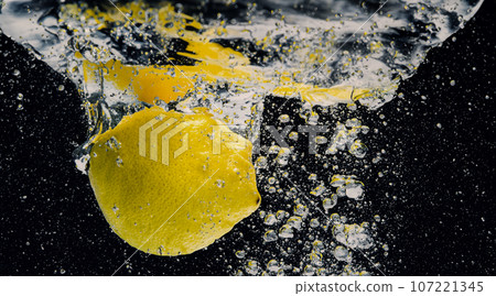 Underwater of freshly squeezed sweetened lemonade which raw lemons slice falling in soda water against dark blue or black background. Close up lemonade or Highball lemon cocktail cold refreshing drink Underwater of freshly squeezed sweetened lemonade which raw lemons slice falling in soda water against dark blue or black background. Close up lemonade or Highball lemon cocktail cold refreshing drink 107221345