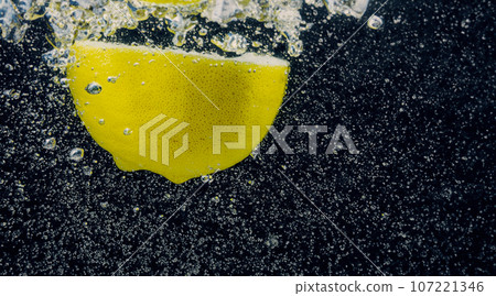 Underwater of freshly squeezed sweetened lemonade which raw lemons slice falling in soda water against dark blue or black background. Close up lemonade or Highball lemon cocktail cold refreshing drink Underwater of freshly squeezed sweetened lemonade which raw lemons slice falling in soda water against dark blue or black background. Close up lemonade or Highball lemon cocktail cold refreshing drink 107221346
