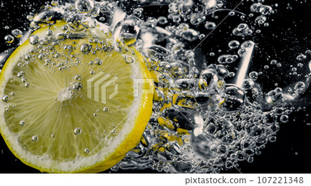 Underwater of freshly squeezed sweetened lemonade which raw lemons slice falling in soda water against dark blue or black background. Close up lemonade or Highball lemon cocktail cold refreshing drink Underwater of freshly squeezed sweetened lemonade which raw lemons slice falling in soda water against dark blue or black background. Close up lemonade or Highball lemon cocktail cold refreshing drink 107221348