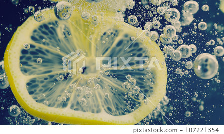 Underwater of freshly squeezed sweetened lemonade which raw lemons slice falling in soda water against dark blue or black background. Close up lemonade or Highball lemon cocktail cold refreshing drink Underwater of freshly squeezed sweetened lemonade which raw lemons slice falling in soda water against dark blue or black background. Close up lemonade or Highball lemon cocktail cold refreshing drink 107221354