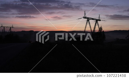 high voltage, Rural infrastructure, Tower plains. Steel pylons holding up power lines cut stark silhouette against sunrise over rural fields. high voltage, Rural infrastructure, Tower plains. Steel pylons holding up power lines cut stark silhouette against sunrise over rural fields. 107221438