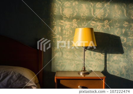 dimmed table lamp casting shadow on a bedroom wall 107222474