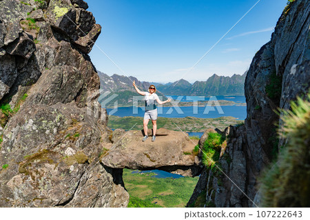 Brave traveler woman standing on hanging stone between rocks. Djevelporten in Norway Lofoten islands 107222643