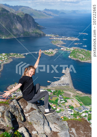 Happy young girl hiker enjoys the view on cliff edge of lofoten islands, in Norway, Reinebringen Happy young girl hiker enjoys the view on cliff edge of lofoten islands, in Norway, Reinebringen 107222665