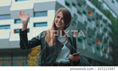 Good looking girl with Long Brown Hair Looking at Her phone Typing and Smiling. Enormous industrial Building at the Background. Green Bushes and Trees. Smart clothes. Natural makeup Good looking girl with Long Brown Hair Looking at Her phone Typing and Smiling. Enormous industrial Building at the Background. Green Bushes and Trees. Smart clothes. Natural makeup 107222997