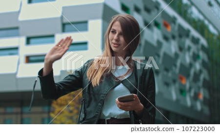 Good looking girl with Long Brown Hair Looking at Her phone Typing and Smiling. Enormous industrial Building at the Background. Green Bushes and Trees. Smart clothes. Natural makeup Good looking girl with Long Brown Hair Looking at Her phone Typing and Smiling. Enormous industrial Building at the Background. Green Bushes and Trees. Smart clothes. Natural makeup 107223000