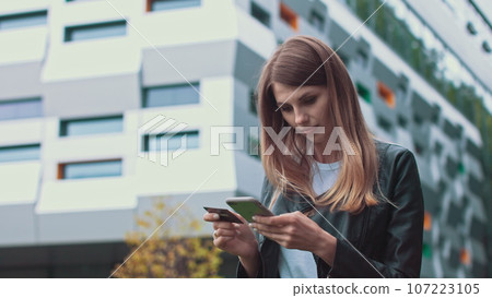 Smiling young female customer holding credit card and smartphone, on modern home background. Happy women shoppers using instant simple mobile payments while shopping online. Electronic banking service 107223105