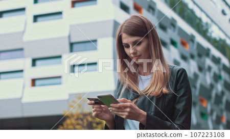 Smiling young female customer holding credit card and smartphone, on modern home background. Happy women shoppers using instant simple mobile payments while shopping online. Electronic banking service 107223108