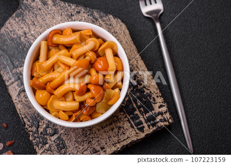 Delicious pickled honey mushrooms with salt and spices in a ceramic plate 107223159