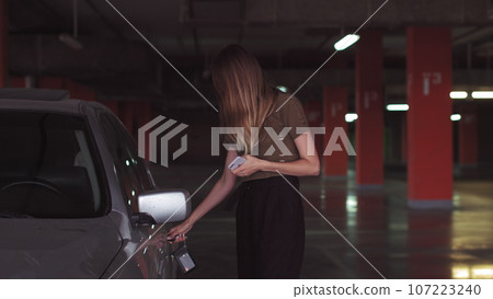 An attractive woman uses a key to open a car in an underground parking lot. A good-looking girl opens the car An attractive woman uses a key to open a car in an underground parking lot. A good-looking girl opens the car 107223240