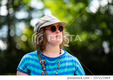 Outdoor portrait of a 40 yo woman with the Down Syndrome, wearing sunglasses and a hat, Belgium 107223964