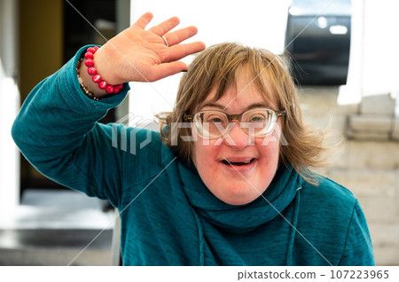 Portrait of a cheerful 40 yo woman with the Down Syndrome waving and smiling, Belgium 107223965
