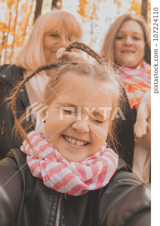 Mother, grandmother and little granddaughter with jack russell terrier dog taking selfie by smartphone outdoors in autumn nature. Family, pets and generation concept 107224110