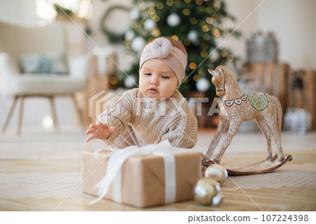 Pretty little girl sitting near gift box over Christmas tree 107224398
