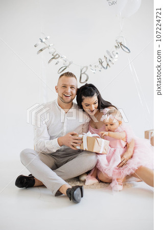 Baby girl unwrapping birthday present with happy parents Baby girl unwrapping birthday present with happy parents 107224721