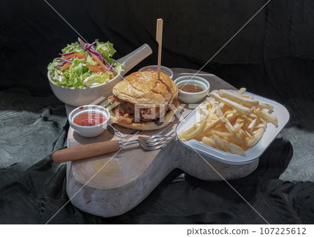 Pork burger with white sesame seeds with French fries potatoes and Salad served with ketchup sauce, mayonnaise and salad dressing. Pork burger with white sesame seeds with French fries potatoes and Salad served with ketchup sauce, mayonnaise and salad dressing. 107225612