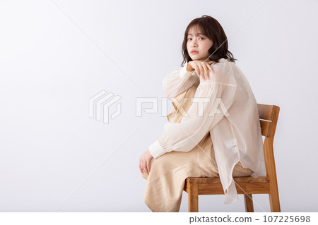 A woman in a dress sitting on her knees on a chair 107225698