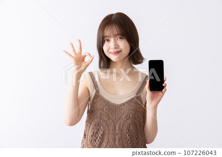 一名年輕女子拿著智慧型手機並給予 OK 手勢 107226043