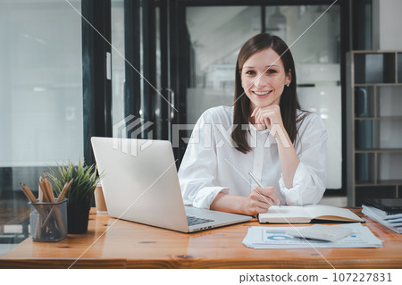 Successful businesswoman sitting in creative office and looking at camera. Woman entrepreneur in a coworking space smiling.. 107227831