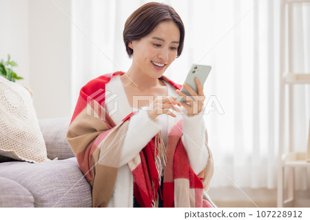 Portrait of a woman sitting on a sofa and looking at her smartphone Portrait of a woman sitting on a sofa and looking at her smartphone 107228912