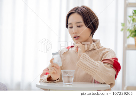 Unwell, woman looking at medicine bottle 107229265