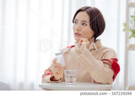 Unwell, woman looking at medicine bottle Unwell, woman looking at medicine bottle 107229266