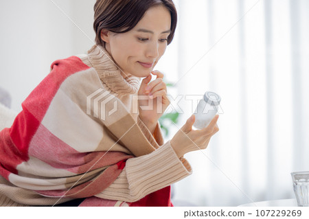 Unwell, woman looking at medicine bottle 107229269