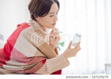 Unwell, woman looking at medicine bottle 107229270