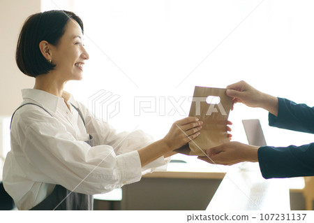 A woman in her 40s passing a paper bag 107231137