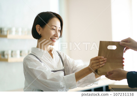 A woman in her 40s passing a paper bag 107231138