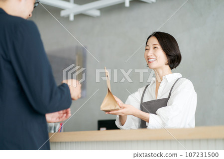 A female clerk handing over a paper bag 107231500