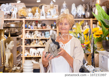Mature woman choosing decorative statue at shop Mature woman choosing decorative statue at shop 107231997