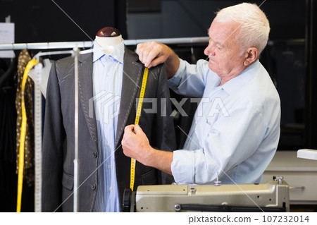 Mature male tailor takes measurement from his jacket using measuring tape Mature male tailor takes measurement from his jacket using measuring tape 107232014