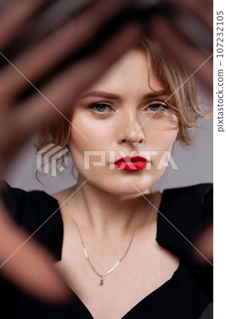 Red-lipped woman in black dress, looks at the camera. 107232105