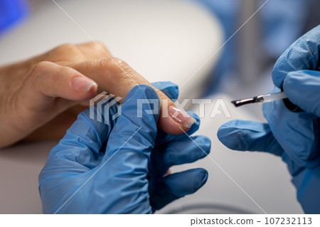 Nail care procedure in a beauty salon. Female hands and tools for manicure, process of performing manicure in beauty salon. Concept spa body care. Gloved hands of a skilled manicurist cutting cuticles Nail care procedure in a beauty salon. Female hands and tools for manicure, process of performing manicure in beauty salon. Concept spa body care. Gloved hands of a skilled manicurist cutting cuticles 107232113
