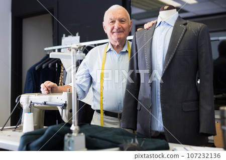 Experienced tailor tries on a new jacket on a mannequin in workshop Experienced tailor tries on a new jacket on a mannequin in workshop 107232136